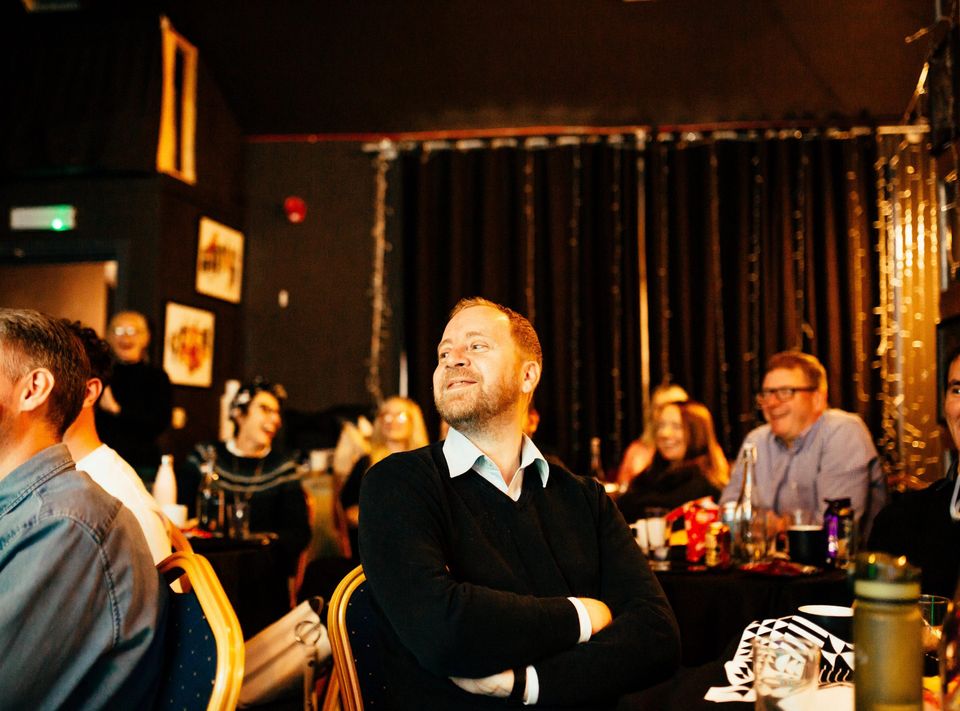 group of people sat a tables looking a at a screen and smiling
