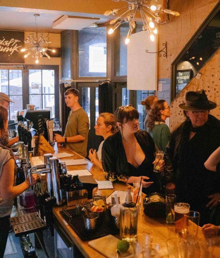 group of people standing at the bar waiting to be served and talking to bar staff
